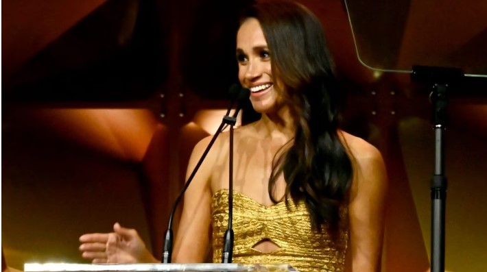 Meghan Markle torna sul red carpet con Harry e mamma Doria: veste d’oro col tubino cut-out